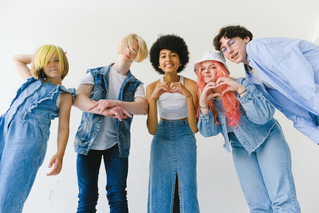 A group of happy, diverse teenagers posing in denim outfits, making heart gestures in a studio setting.